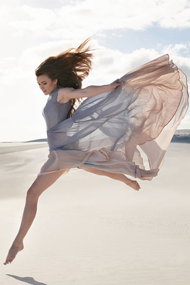 A woman in a long dress is jumping on the sand at a beach