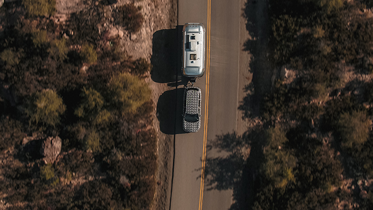 A aerial shot of a QX60 pulling a large silver trailer across a country road