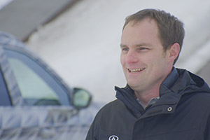 Un homme vêtu d'une veste noire debout devant l'INFINITI QX60 dans la neige.