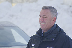 Un homme vêtu d'une veste noire debout devant une voiture INFINITI recouverte de neige.