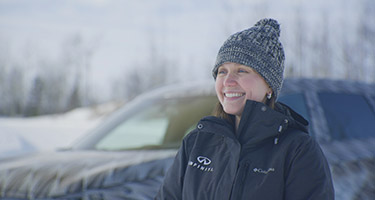 A woman in a black jacket standing in front of the INFINITI QX60 in the snow.